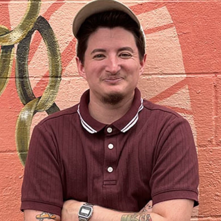 Cas Brown, archivist, in a cap and dark polo in front of an orange mural wall