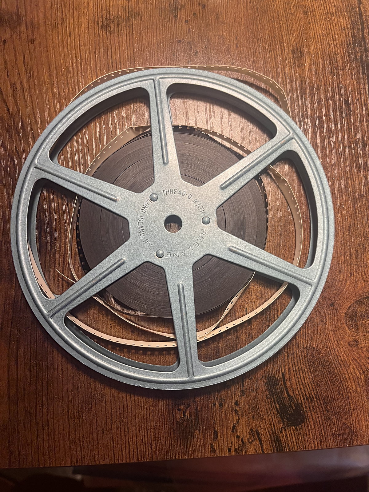 A silver metal reel with film wound on, lying flat on a dark oak table.